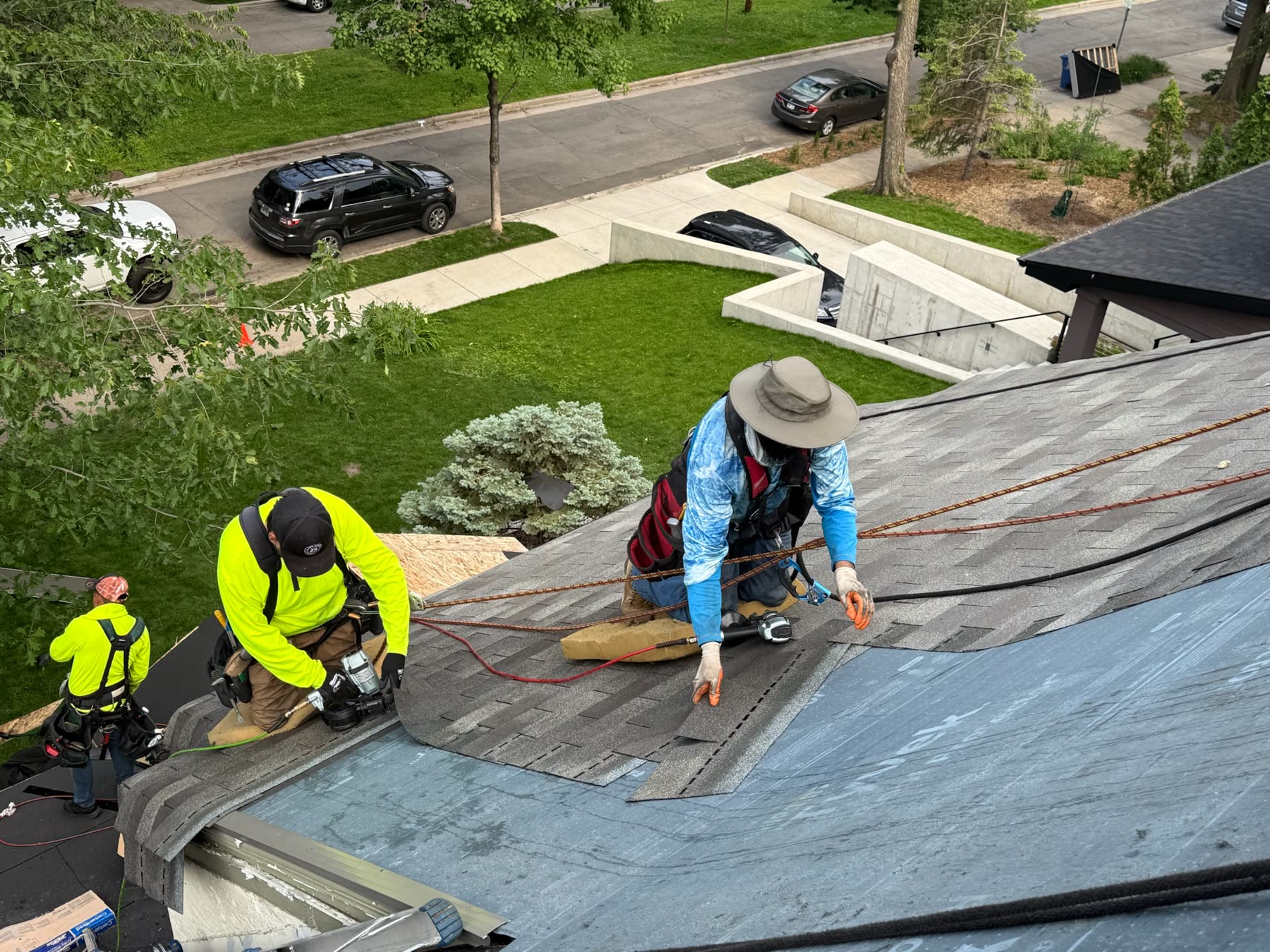 A Stoneridge crew laying new shingles on a Twin Cities roof, with the street and yard below